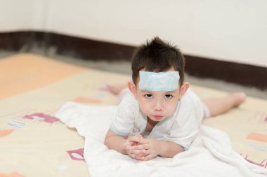 Ateşi olan Asyalı bir çocuk. Çocuk rahatlamak için alnına soğutucu jel pedi yapıştırmış.