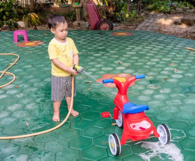 Asyalı bebek, yeşil su püskürtücüsüyle kırmızı bisikleti yıkıyor.