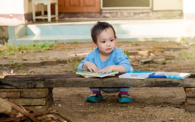 Asyalı bebek dışarıda masal okuyor.