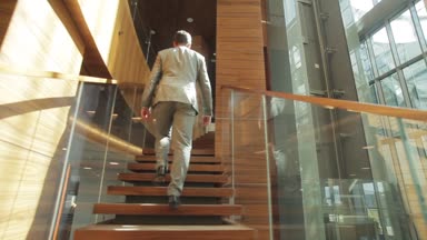 İş adamı merdivenlerden geri düşük açılı görünümü modern ahşap cam iç ferah evine. Adam giyen iş giysileri artan tırmanma üst kat ofis daire uygun. Bina tasarım stili