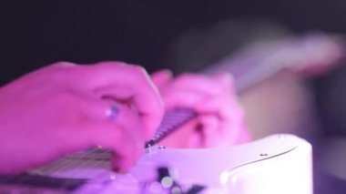 Gitarist eller makro yakın çekim elektrik ağır çekim neon ışık gece klübünde oynamaktadır gitar dizeleri koparma parmakları. Müzisyen adam yapar solo acil akorları konser ilham prova grubu