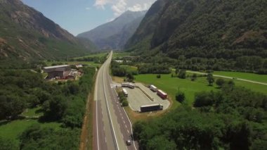 Kamyon kamyonet kamyon kırsal otopark ile uçan geriye doğru iki şeritli karayolu robot. 4k hava pan bakışı dağlar otoyol yeşil yamaçları gökyüzü arka planda Avrupa şehrin kuşlar