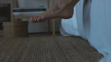 Yüzsüz kadın sabah yaşam tarzı doğal ışık iç yakından yataktan kalkmak. Kadın ayakları yatak odası hasır halı mobilya uyanma yere basarak. Hangover uykusuzluk flatfoot işe geç