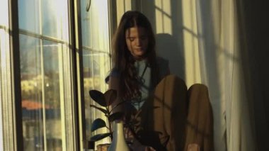 Kadınsı kız pencere açıklarında ev iç 4k oturan güneş ışığı zevk. Gündelik kıyafetler içinde zarif kadın güneşe gülümseyerek pencere tarafından tek başına rahatlatıcı. Yakın yaşam tarzı insanlar portre boş zaman