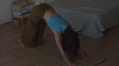 Güzel uzun saçlı kız Yoga kapalı karanlık iç arka plan 4k el kamera pratik. Gün doğal ışık germe Asana içinde duran genç kadın. Güneş selamlama sırası Surya Namaskar