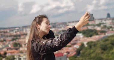 Şık kız akıllı telefon kameraya doğal gün ışığı açık gülümseyerek selfie fotoğraf yapma. Cityscape arka plan çatı ufuk el kamera poz genç mutlu kadın. Kadın moda güzellik sağlıklı yaşam