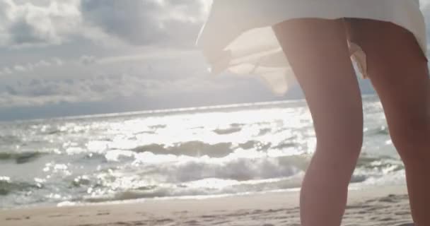 女性旋转在白色裙子快乐在海边特写前看阳光明媚的夏日 无脸女性腿旋转飞舞的礼服在波光粼粼的海洋背景慢动作幸福 — 图库视频影像