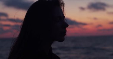 Doğal akşam ışığında deniz kenarında hayal kapalı gözleri ile arkadan aydınlatmalı kız yakın yan portre. Renkli gökyüzü arka planda deniz plajında tek başına meditasyon rahatlatıcı genç kadın. Stres üstesinden