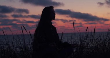 Karanlık akşam ışık el cihazı açık havada meditasyon kız ön görünüm portre. Siluetli yogini kadın doğa sahil arka plan üzerinde kapalı gözleri ile çapraz bacaklı oturuyor. Din inancı
