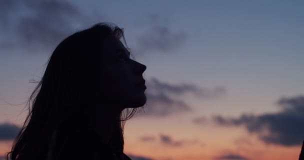 夏の夜のスローモーションを楽しんで空を見上げる長髪の女性の暗いプロフィール 夕日の背景に一人でリラックスシルエットの女の子のサイドポートレート 瞑想ウェルネスストレス克服 — ストック動画