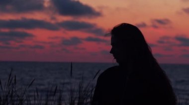 Pembe günbatımı arka plan üzerinde kapalı gözleri ile deniz kenarında poz doğal kız Yan görünüm portresi. Genç kadın rahatlatıcı meditasyon açık havada siluet yükselen güneş el cihazı yavaş hareket ayarı tarafından siluet