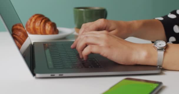 紧紧抓住女性的手 在笔记本电脑键盘上放上咖啡角面包放在背景上 在室内电脑上工作的无脸女人侧视慢动作 自由经商的企业家 — 图库视频影像