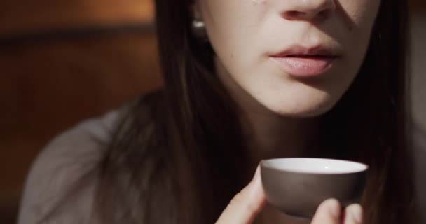 Dolní polovina portrétu dívky popíjející čaj z malého černého kelímku v interiéru přirozené sluneční světlo zpomaluje. Detailní zblízka tvář rty ženy držící stylový šálek čaje kopírovat prostor 4k. Degustační proces
