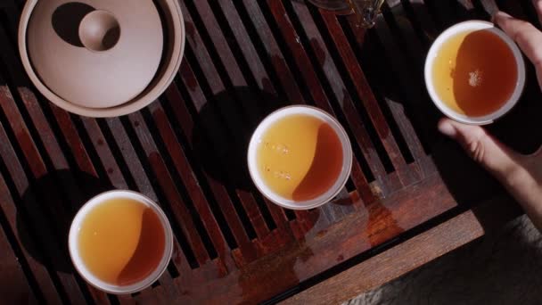 木製の竹の机のテーブルを閉じる熱いお茶でいっぱいのお茶を飲む人の手のトップビュー 顔のない男性は 中国の発酵飲料伝統的な東洋の儀式を飲む 東洋のライフスタイルヘルスケア — ストック動画