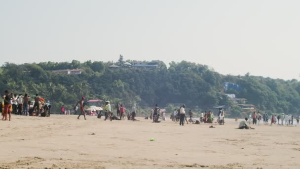 GOKARNA, INDIA-20 DE FEBRERO DE 2020: Turistas caminando por la playa de arena en el caluroso día de verano en cámara lenta. Muchas personas se relajan al aire libre en el fondo tropical junto al mar. Vacaciones turísticas de viaje verano — Vídeo de stock