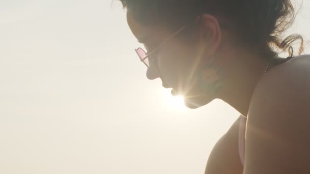 Close-up vista lateral da mulher em óculos de sol no fundo do céu branco espaço de texto cópia iluminada pelo sol. Perfil retrato de menina bonita posando ao ar livre retroiluminado com sol brilhando. Produtos femininos de beleza — Vídeo de Stock