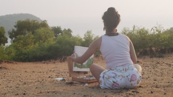 Vista posterior de artista joven pintura al aire libre en las montañas fondo cámara lenta. Mujer sentada con lienzo y herramientas de arte trabajando sola en la naturaleza. Proceso creativo meditación relajación — Vídeo de stock