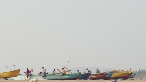 GOKARNA, INDIA-FEBRERO 02,2020: pescadores indios de pie en botes coloridos preparándose para navegar en cámara lenta. Personas irreconocibles que trabajan al aire libre en la playa caliente verano día copia espacio de texto — Vídeo de stock