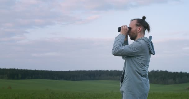 緑のフィールドの背景コピースペースのフィールドガラスを調べる本物の男。野生の自然のスローモーションで動物を観察旅行者の側のビュー。動物園保護職業概念 — ストック動画