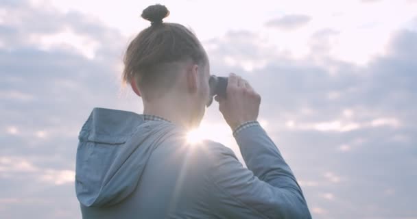 夏のトレッキングの旅の自然光のヘアスタイルを持つ男の観光客。双眼鏡のコピーテキストスペースで自然を見て男のビューを閉じます。アクティブなライフスタイル夏休み — ストック動画