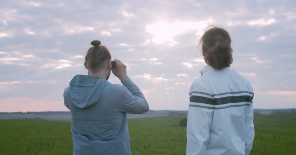 Dürbünle yeşil alan manzarasında duran vahşi doğa hayvanlarını izleyen iki arkadaş. İki adam kırsal alanda el kamerası olan bir yere bakıyor. Turizm yaz aktif yaşam tarzı — Stok video