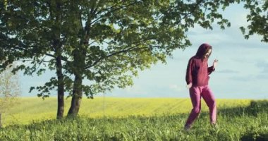 Neşeli kız sabah dışarıda dans ediyor. Doğal aydınlık doğa arka planında. Kapüşonlu spor elbiseli genç bir kadın ağır çekimde hareket ediyor. Özgürlüğün kurtuluşu, refahın stresi