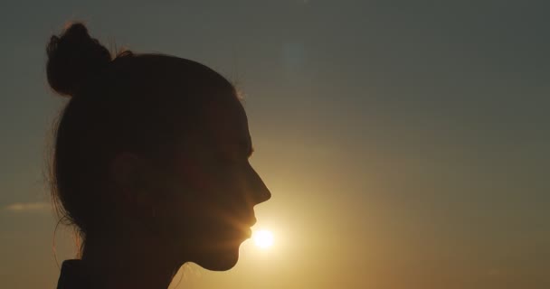 Retrato lateral da menina com coque beijando sol ao ar livre no fundo de luz dourada noite perto. Belo perfil feminino silhueta no céu sunset cópia espaço de texto câmera lenta. Verão de felicidade — Vídeo de Stock