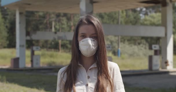 Portrait of young woman wearing protective virus mask on abandoned industrial background. Front view of girl standing alone outdoors on quarantine street. Pandemic covid health protection concept — Stock Video