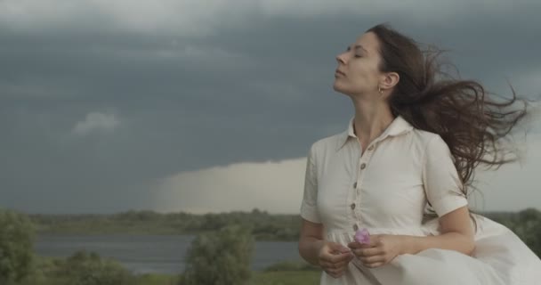 Headshot portret van meisje ademen frisse wind op regenachtige stormachtige lucht achtergrond. Serieuze vrouw staan met blazen fladderend haar outdoor slow motion kopie tekstruimte. Milieubescherming — Stockvideo