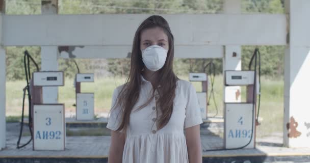 Feche o retrato da jovem mulher de pé na rua vazia apenas com máscara protetora. Menina posando no fundo abandonado posto de gasolina durante a pandemia gripe vírus covid câmera lenta. Protecção médica — Vídeo de Stock