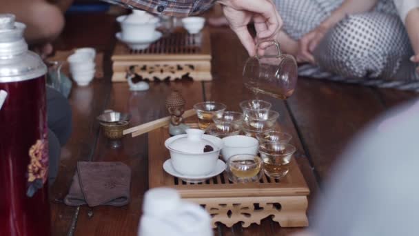 Вид сбоку на безликого человека, заваривающего горячий чай в стеклянных чашках в помещении замедленной съемки. Процесс китайской церемонии закрыть лицо естественного света. Инструменты восточной культуры отступают дегустация — стоковое видео