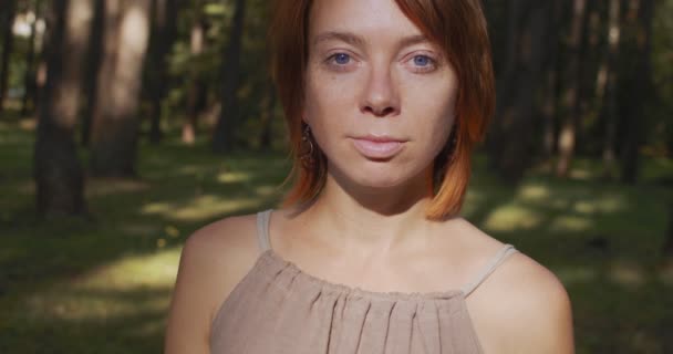 Portræt af rødhårede pige med blå øjne poserende udendørs på naturen baggrund slow motion. Front visning af naturlige kvinde uden make-up ser alvorlig i grøn skov. Hud skønhed pleje produkter – Stock-video
