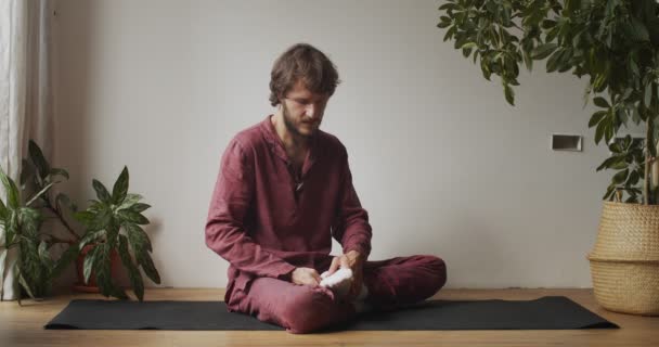 Vue de face du maître de massage thaï démontrant les principes à l'intérieur de la lumière naturelle. Homme masseur assis sur tapis de yoga tenant le pied sur maître classe tutoriel au ralenti. Techniques orientales soins de santé — Video