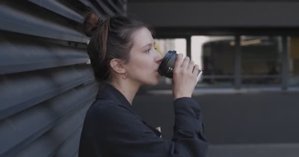 Boční pohled na šťastnou dívku pití kávy venku na městském pozadí zpomalení. Portrét přirozené ženy držící jednorázové papírové kelímek s čajem těší život na ulici. Pozitivní životní styl — Stock video