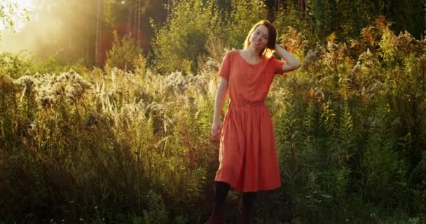 Glad flicka i linne klänning njuter av naturligt solnedgång ljus utomhus på naturen bakgrund. Ung kvinna i vintage kläder poserar i höst fält bakgrundsbelyst genom att sätta solen slow motion. Frihet wellness stil — Stockvideo