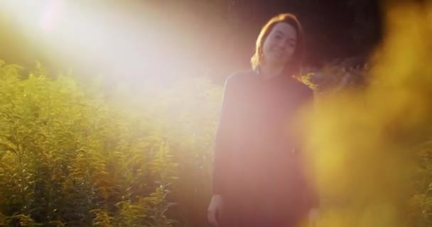 Gelukkig vrouw besteden vrije tijd op zonnige natuur achtergrond slow motion. Ondiep handheld portret van vrolijk meisje genieten van gele bloemen in het veld. Vrijheid vreugde geluk milieu natuur — Stockvideo