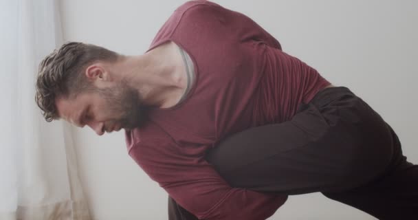 Close up tiro detalhado de homem em pé na postura ioga torcida dentro de casa câmera deslizante. Mestre de iogue concentrado demonstrando asana difícil no fundo do apartamento branco câmera lenta. Corpo flexível — Vídeo de Stock