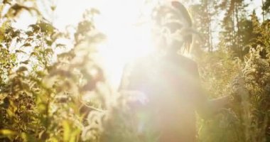 Altın güneş ışığında kuru sonbahar tarlasına çıkan doğal bir kadının el yapımı atmosferik portresi. Kafkasyalı bir kızın doğada tek başına yürümesi. Yavaş çekim ekolojik yaşam tarzını kapat