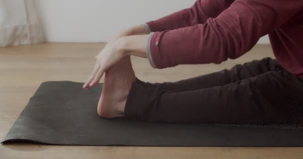 Πλευρική λεπτομερής άποψη του yogi τέντωμα πόδια σε paschimottanasana εσωτερική αργή κίνηση. Μακρο πλάνο των καλλιεργειών του ανθρώπου εξάσκηση hatha γιόγκα μόνη της στο χαλί μέσα στο ηλιόλουστο δωμάτιο. Ευελιξία στον τομέα της υγείας — Αρχείο Βίντεο