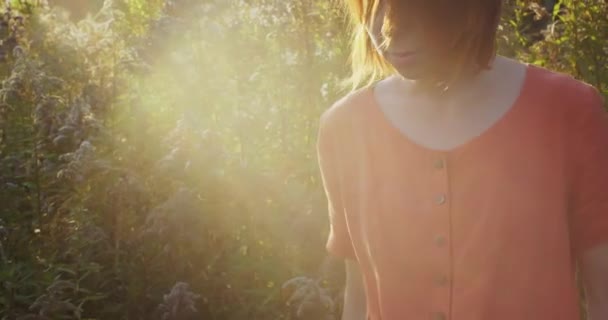 Handheld atmosferisch portret van roodharige vrouw die gelukkig tijd buiten door te brengen op de natuur. Zorgeloos meisje poseren in linnen jurk verlicht door gouden zon licht slow motion. Natuurlijke stijl lifestyle mensen — Stockvideo