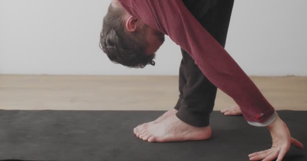 Gros plan vue de la récolte de l'homme étirant les jambes dans uttanasana asana sur tapis à l'intérieur dispositif de poche. Plan latéral détaillé de la personne pratiquant seul le yoga à la maison le matin au ralenti. Activités de soins corporels — Video