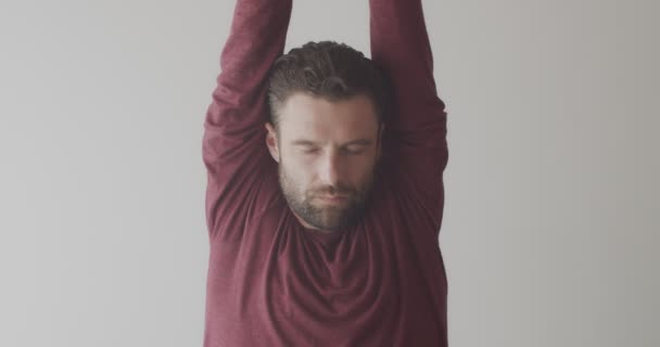 Крупним планом портрет людини, що тримає руки над головою, практикує йогу в приміщенні на білому тлі. Бородатий концентрований майстер йогів розтягує один простір для копіювання природного світла. Духовний здоровий спосіб життя — стокове відео