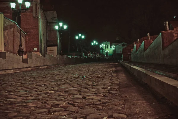 Photo of the old city street road of stones. The road among the houses up at night with lanterns and lights.