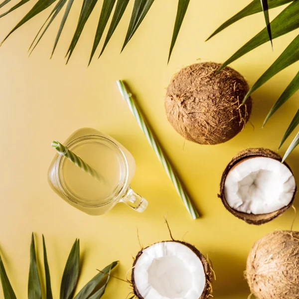 Coconut water and coconuts on a background with tropical leaves.