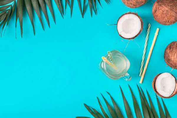 Coconut water and coconuts on a background with tropical leaves.