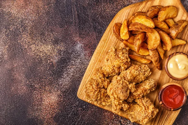 Fried chicken wings with fried potato slices, top view.