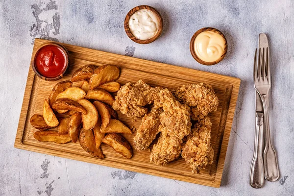 Fried chicken wings with fried potato slices, top view.