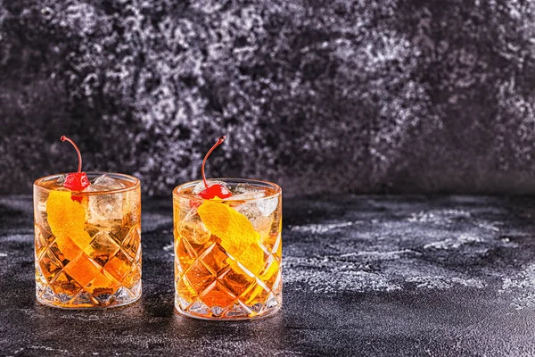 Old fashioned cocktail with cherries and orange twist.