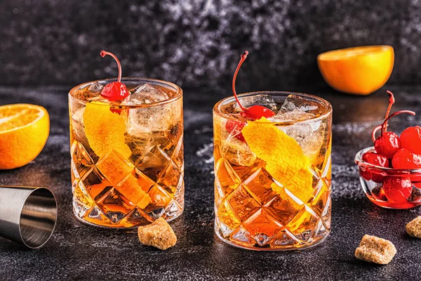 Old fashioned cocktail with cherries and orange twist.