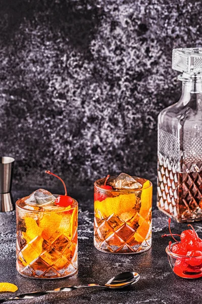 Old fashioned cocktail with cherries and orange twist.